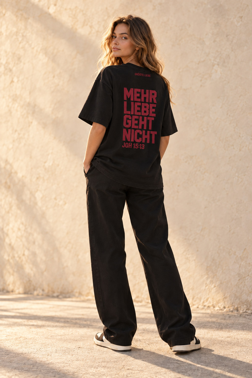 Weibliches Model aus der Naturkampagne mit schwarzem GRÖẞTE LIEBE Signature-T-Shirt und Johannes 15:13 von hinten