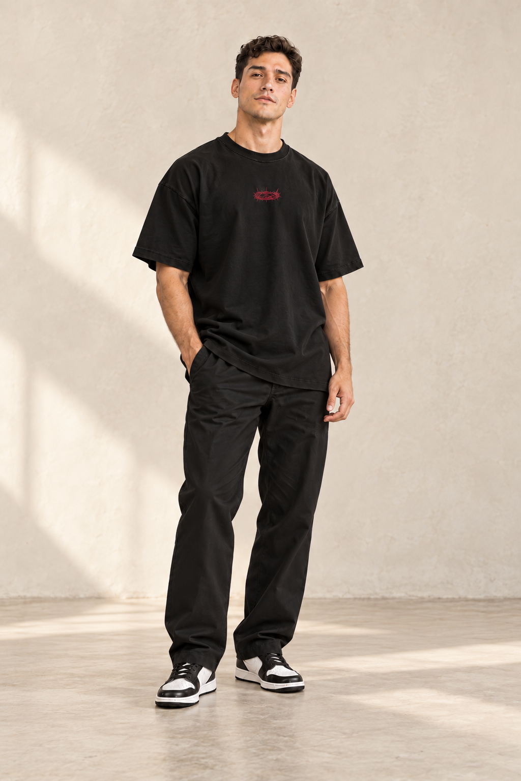 Männliches Model mit schwarzem GRÖẞTE LIEBE Signature-T-Shirt und mittiger bordeauxroter Dornenkrone von vorne